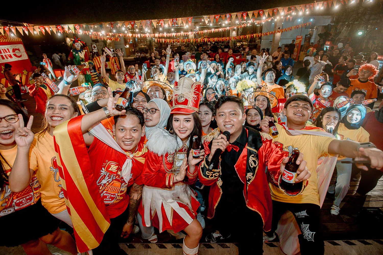Energetic crowd at a sports event wearing red jerseys and cheering under bright stadium lights.