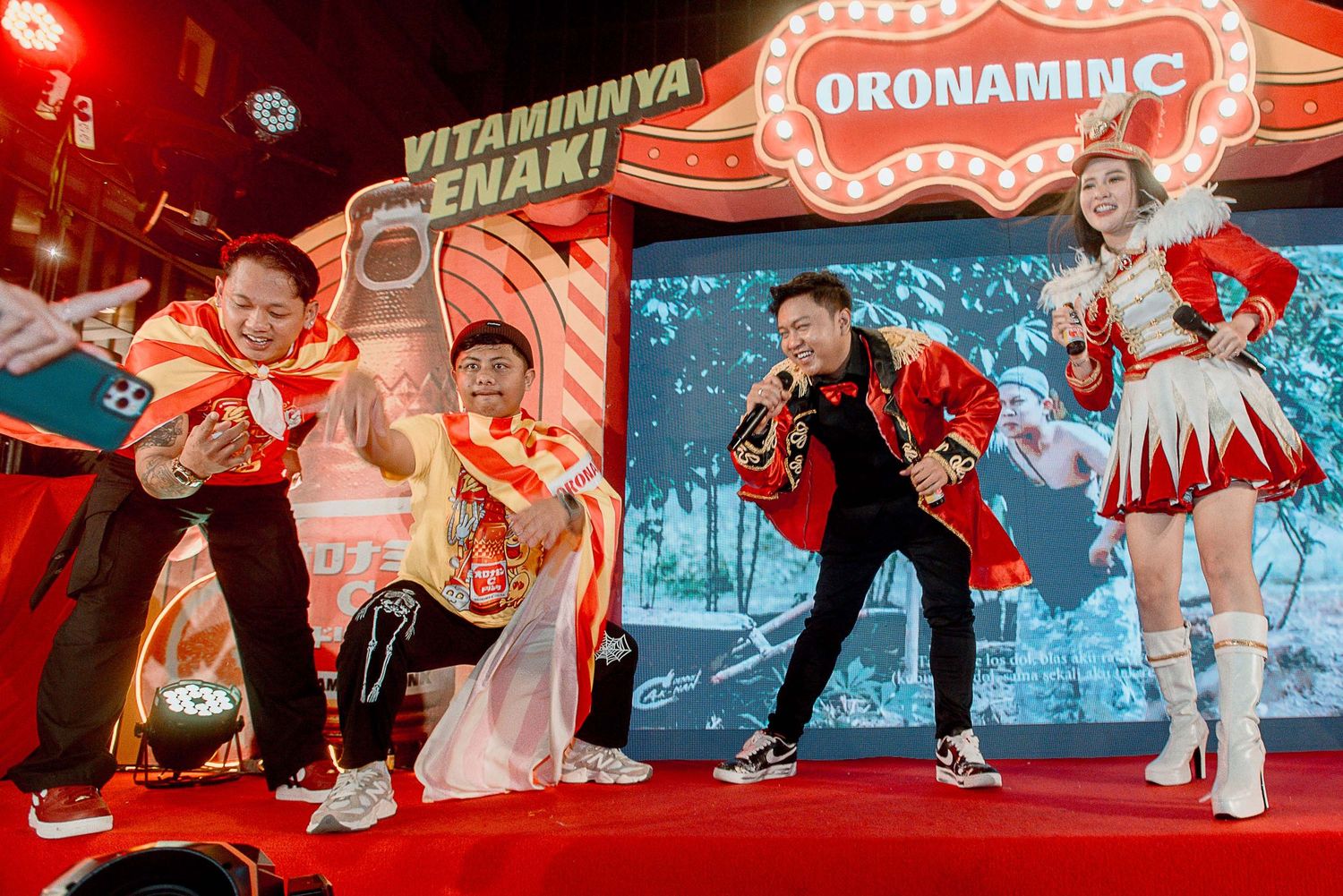 Performers in red and white costumes dance energetically on stage with Japanese signage and decorations in the background.