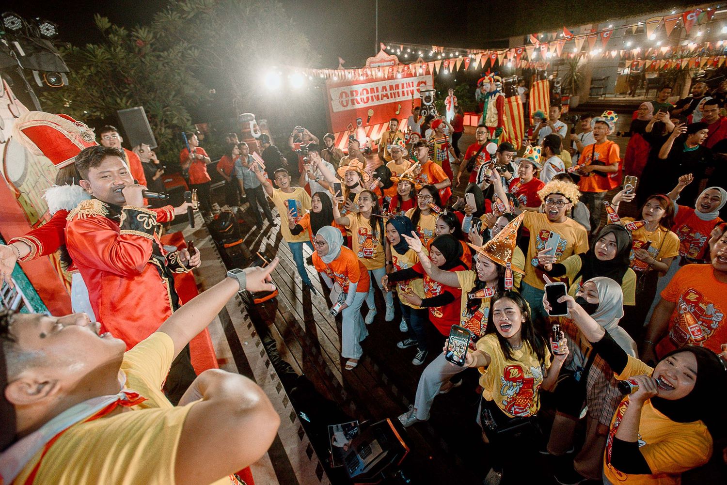 Energetic crowd at a nighttime outdoor event with colorful lights and flags creating a festive atmosphere.