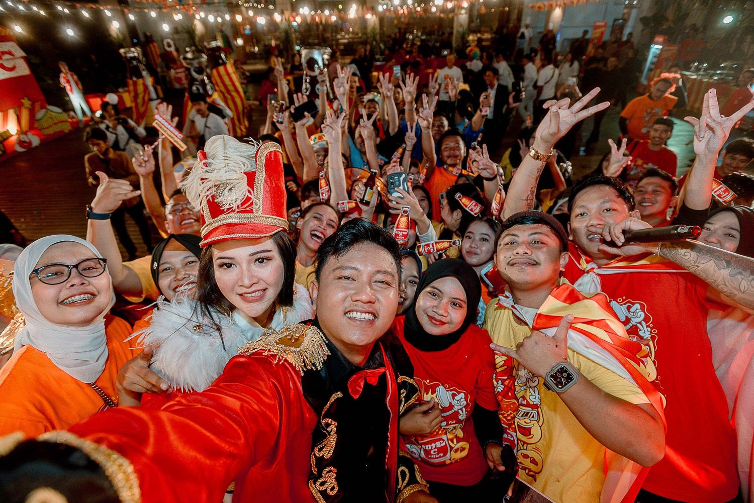 Crowd of sports fans in red jerseys cheering enthusiastically at a sporting event with glowing lights overhead.