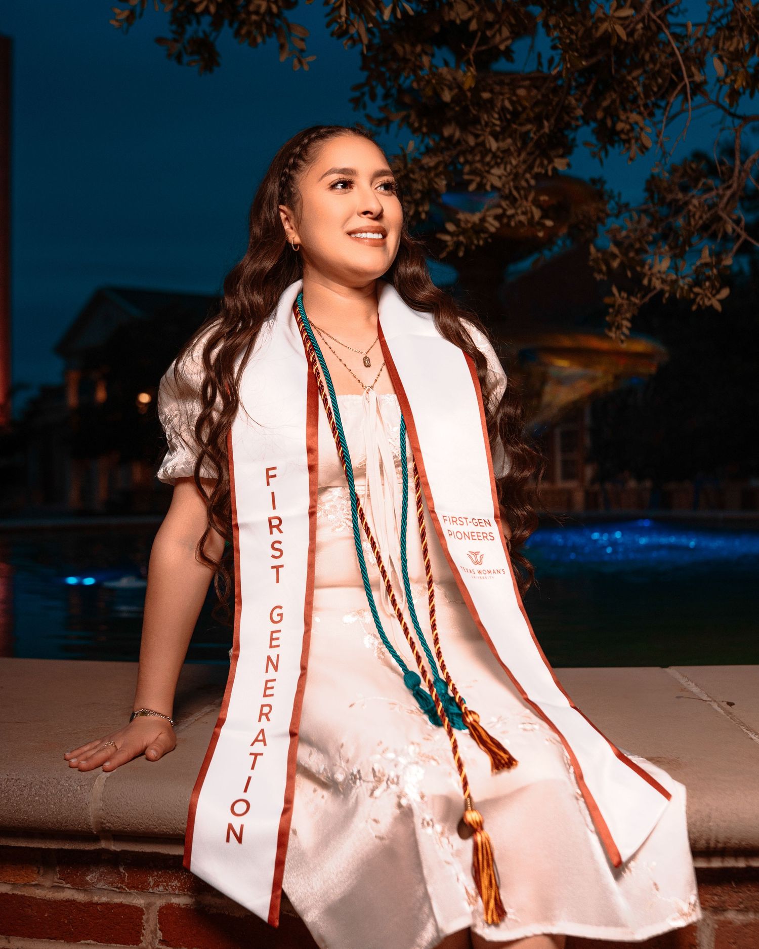 A person wearing a white graduation stole and dress poses in a series of outdoor photos at dusk.