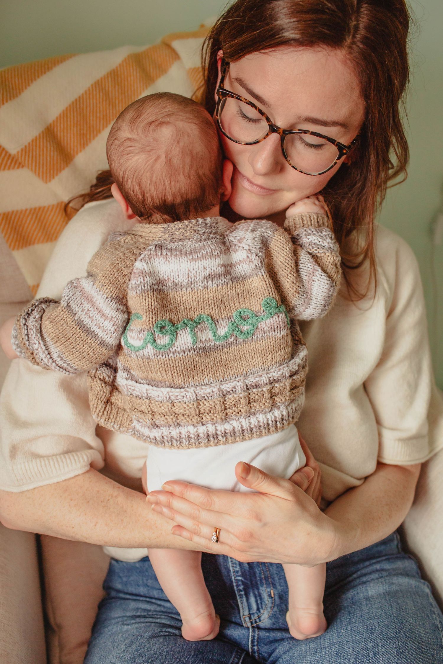 A sleeping baby wearing a cozy knit sweater rests peacefully on a curved white nursing pillow.