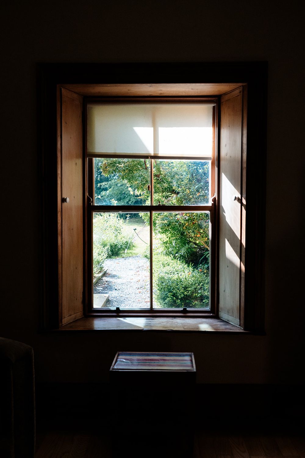 A series of dark interior window frames looking out to bright green garden views through wooden shutters.