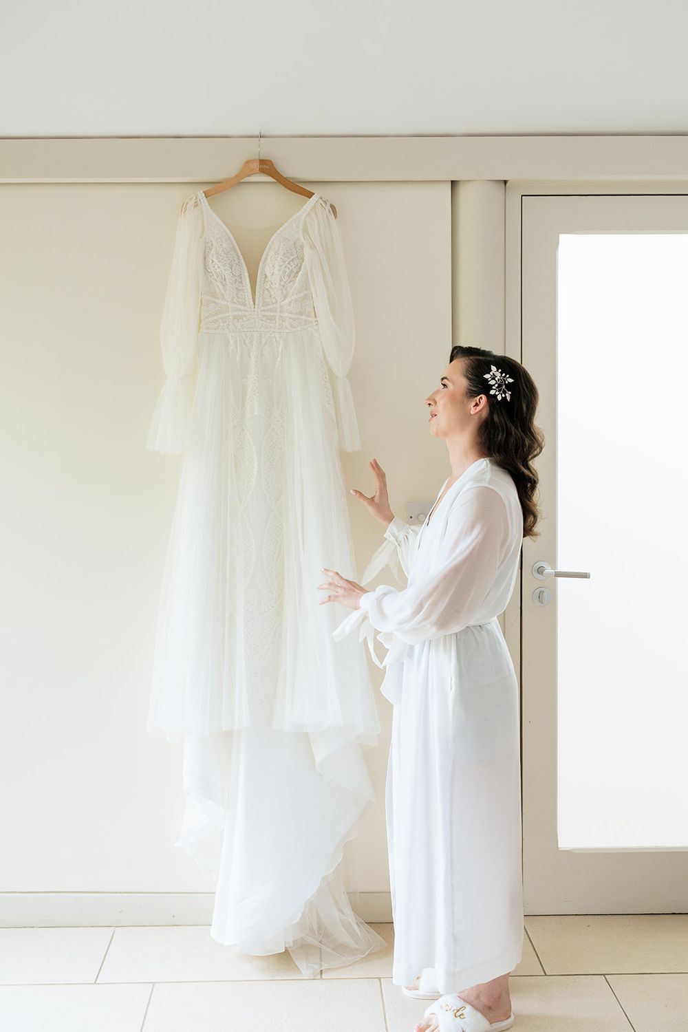 A series of white wedding dresses and robes hanging in a bright minimalist room with natural light.