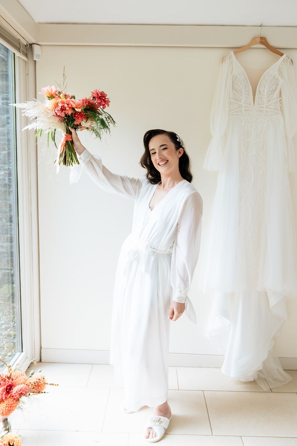 Four minimalist bridal photos showing white wedding dresses hanging in a bright sunlit room with coral flower accents.