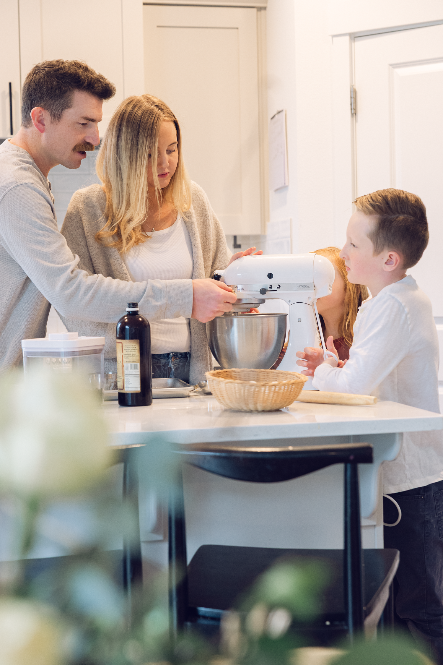 Family of four baking together in a bright kitchen using a stand mixer on a kitchen island.