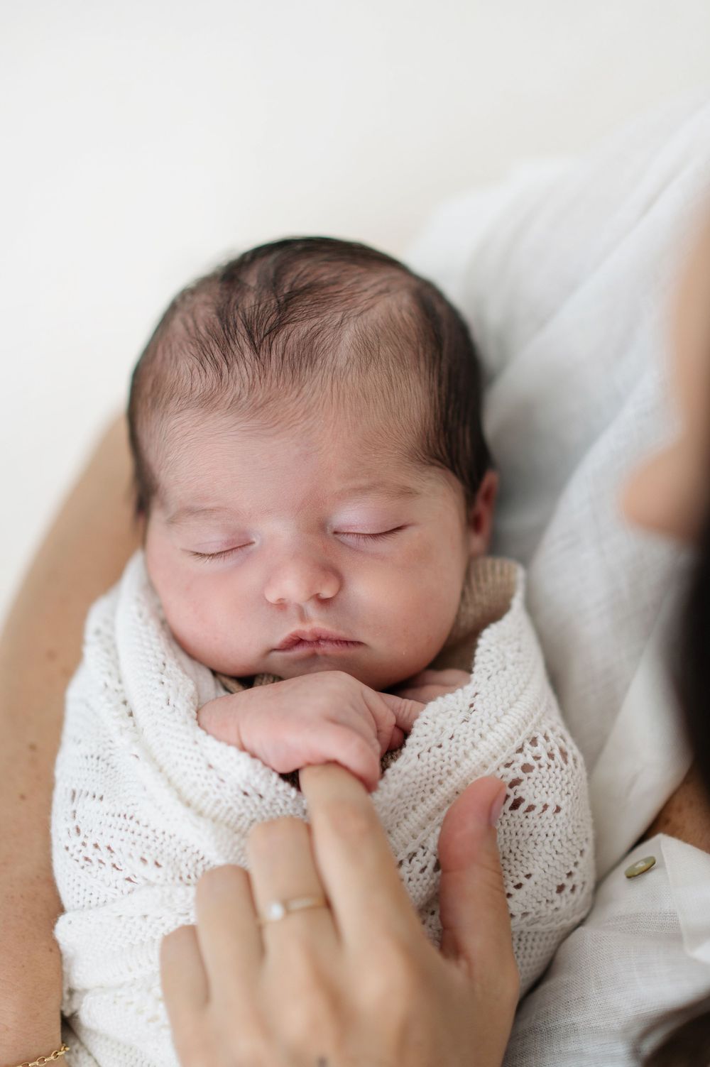 Peaceful sleeping newborn baby wrapped in soft white knit blanket rests against white background.