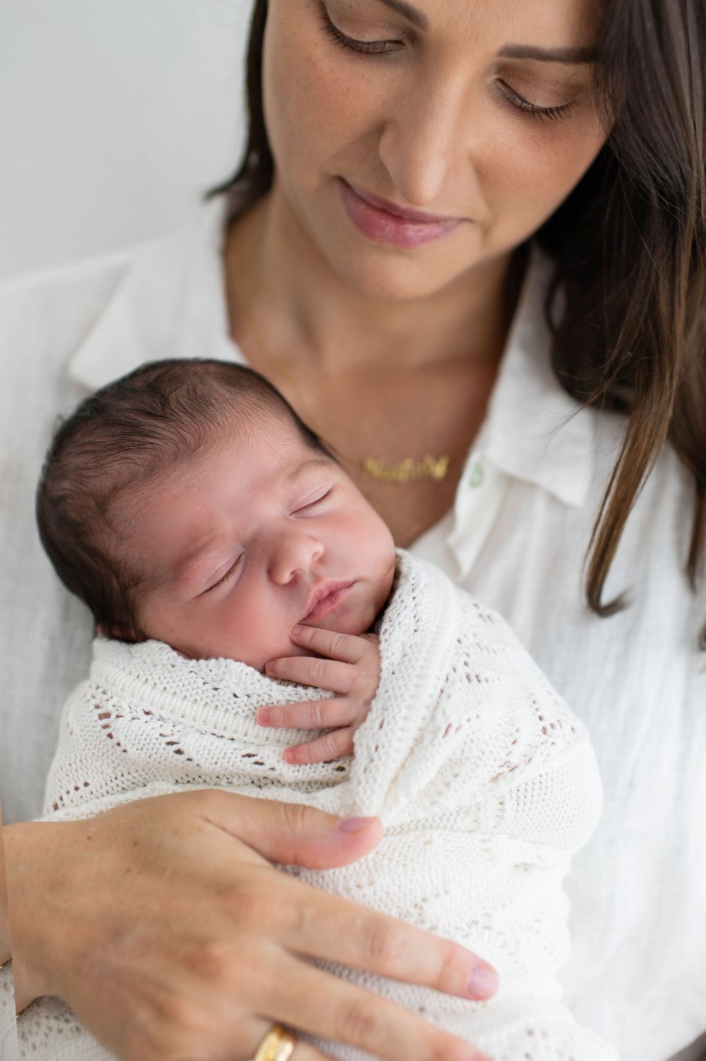 A mother in white holds her sleeping newborn baby wrapped in delicate lace fabric in a series of tender portraits.
