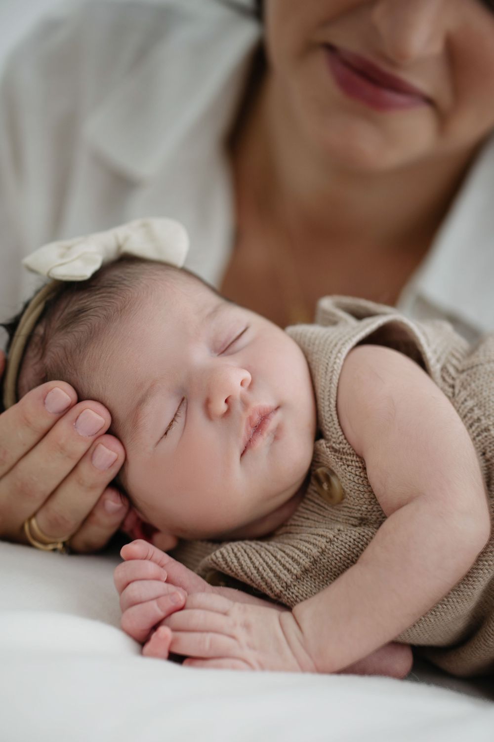 A sleeping baby wearing a knit sweater rests peacefully on white bedding in a series of close-up photos.