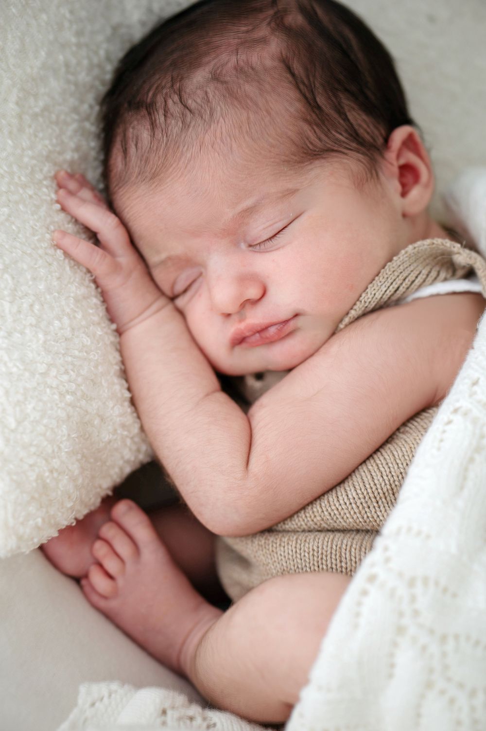 Peaceful sleeping newborn baby wrapped in soft white blanket resting on textured cream fabric.