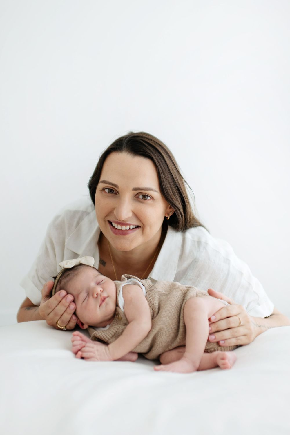 A tender moment between parent and baby lying on white bedding in a bright, minimalist setting.