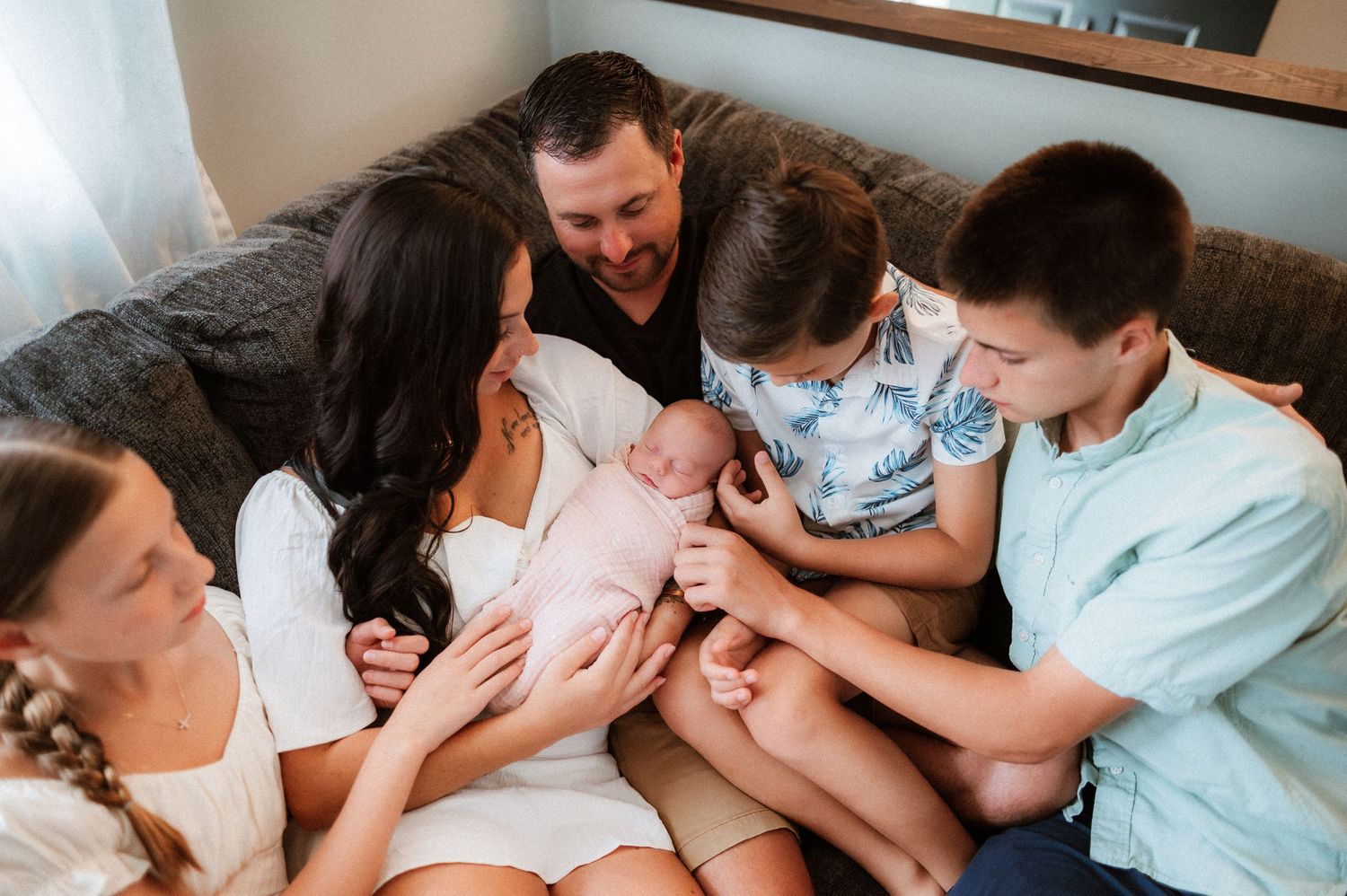 A family lying together on a white couch sharing intimate moments and laughter during a lifestyle photo session.