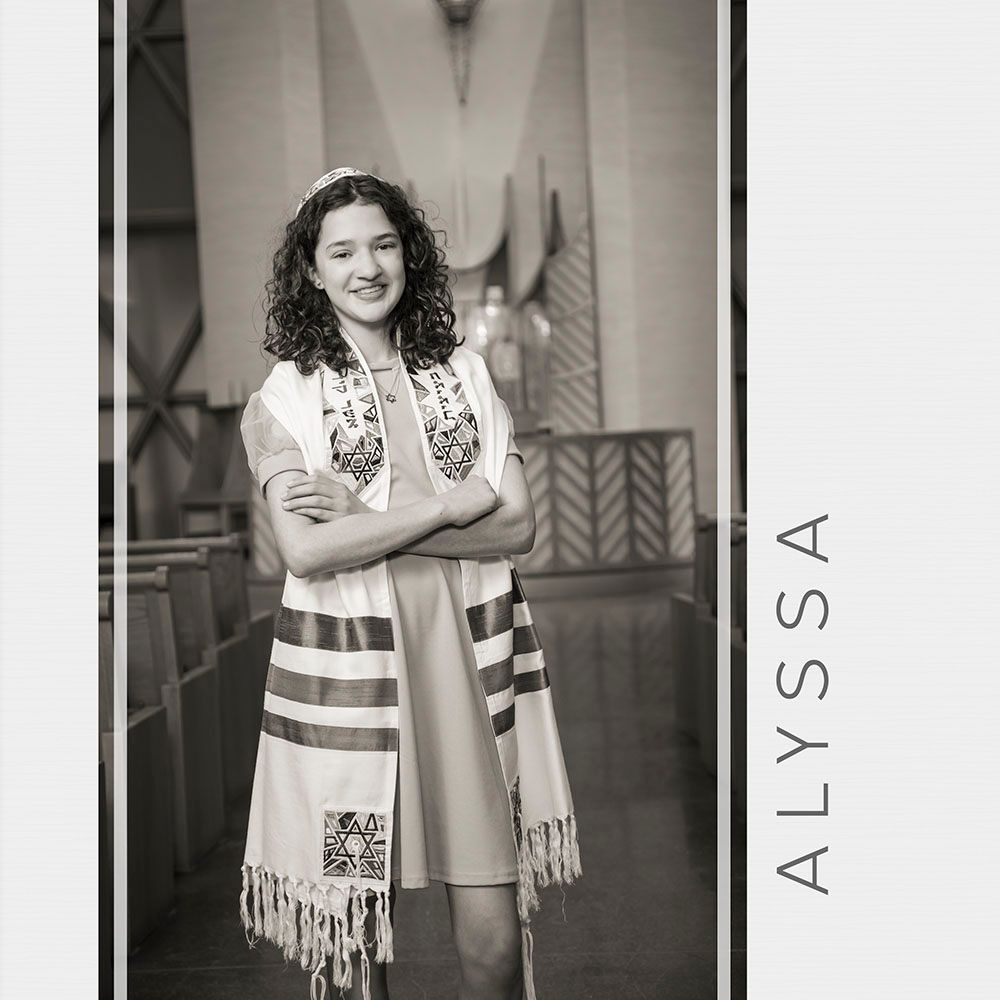 Vintage black and white photograph showing a young person wearing a traditional embroidered shawl in a formal setting.