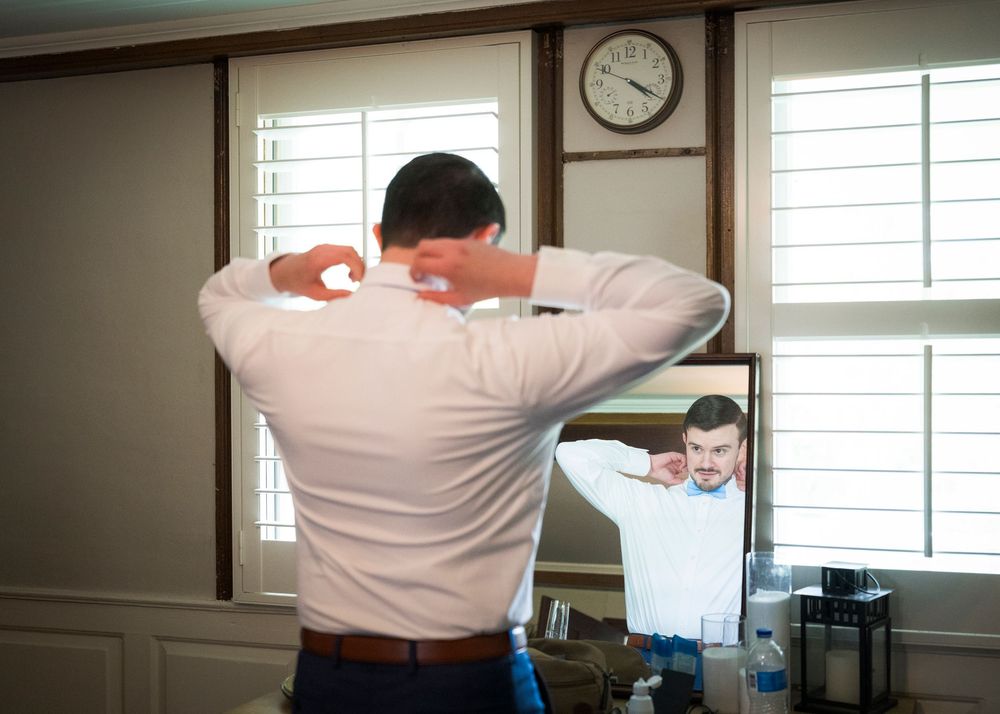 Groom adjusting his collar in a mirror while getting ready for his wedding day.