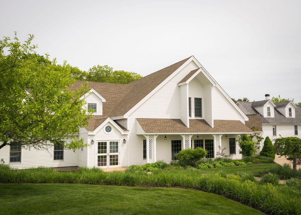 Elegant white farmhouse-style wedding venue surrounded by manicured gardens and lush green lawns.