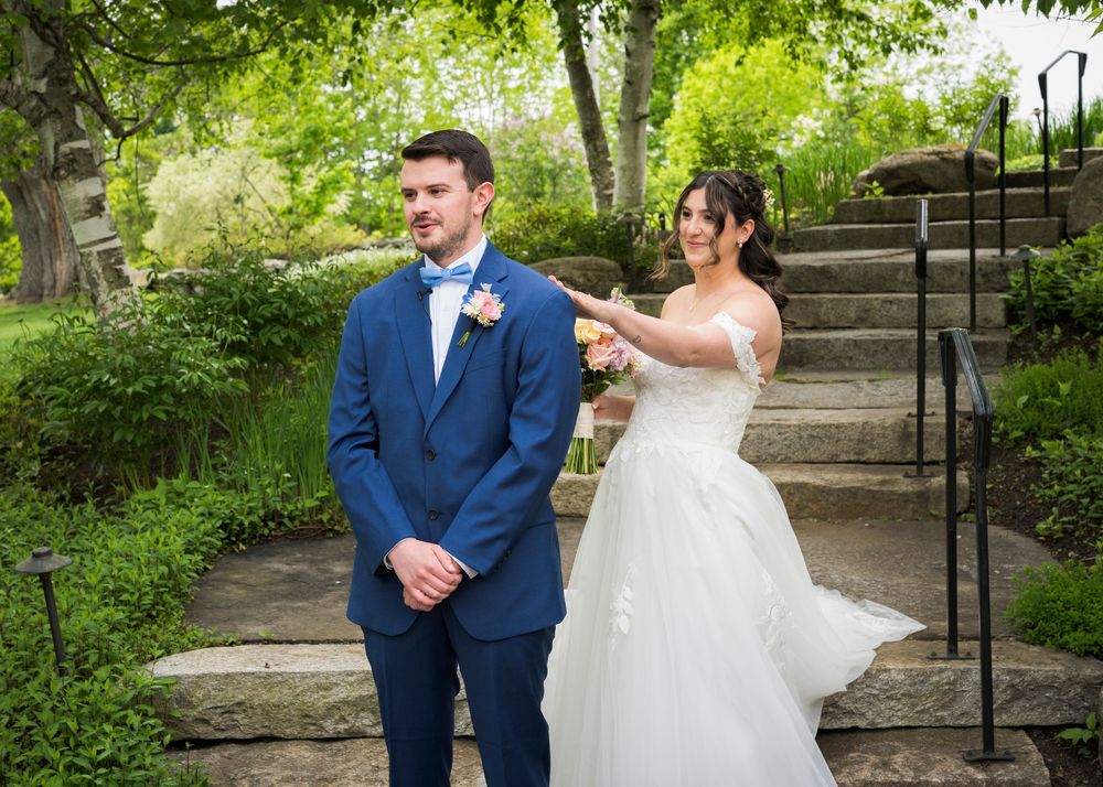 Bride surprises groom from behind during first look moment on garden stone steps.