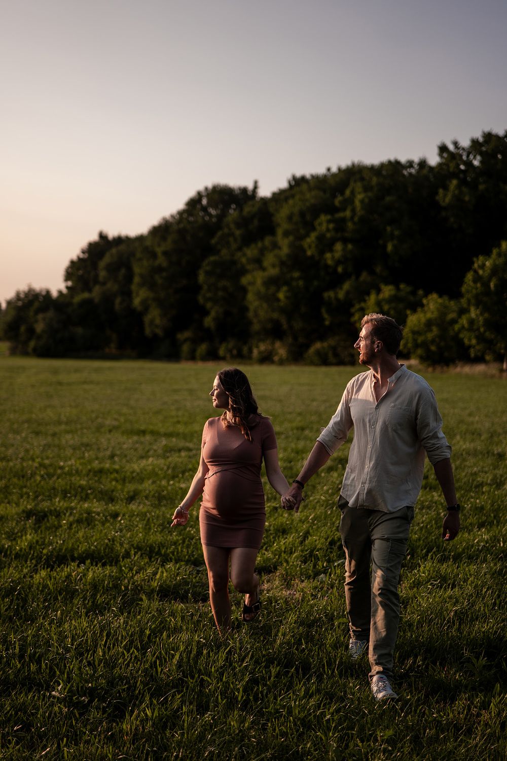 Paar geht Hand in Hand über eine Wiese bei einer entspannten Babybauch-Reportage in NRW.