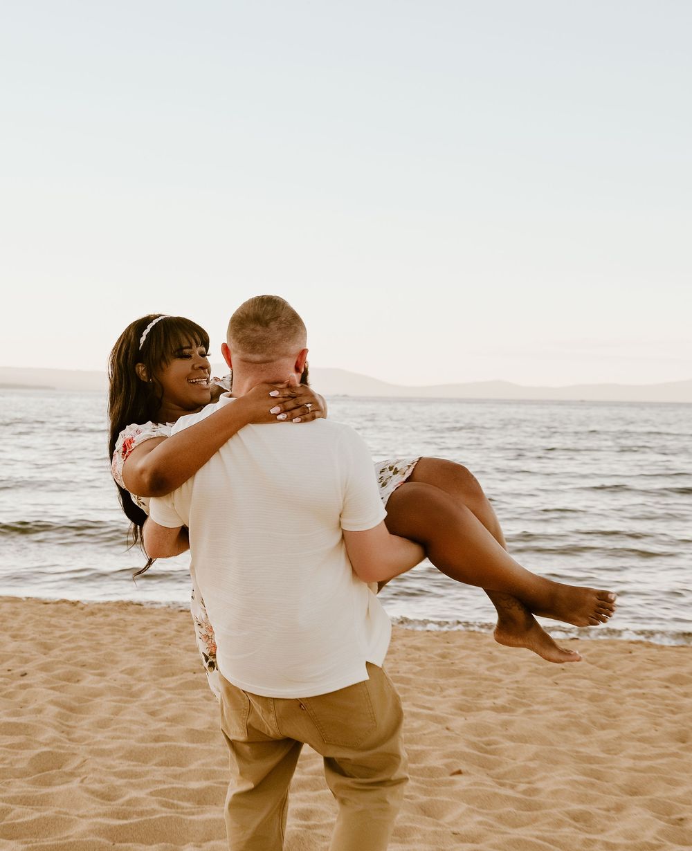 A romantic couple embraces and dances together on a sandy beach at sunset.
