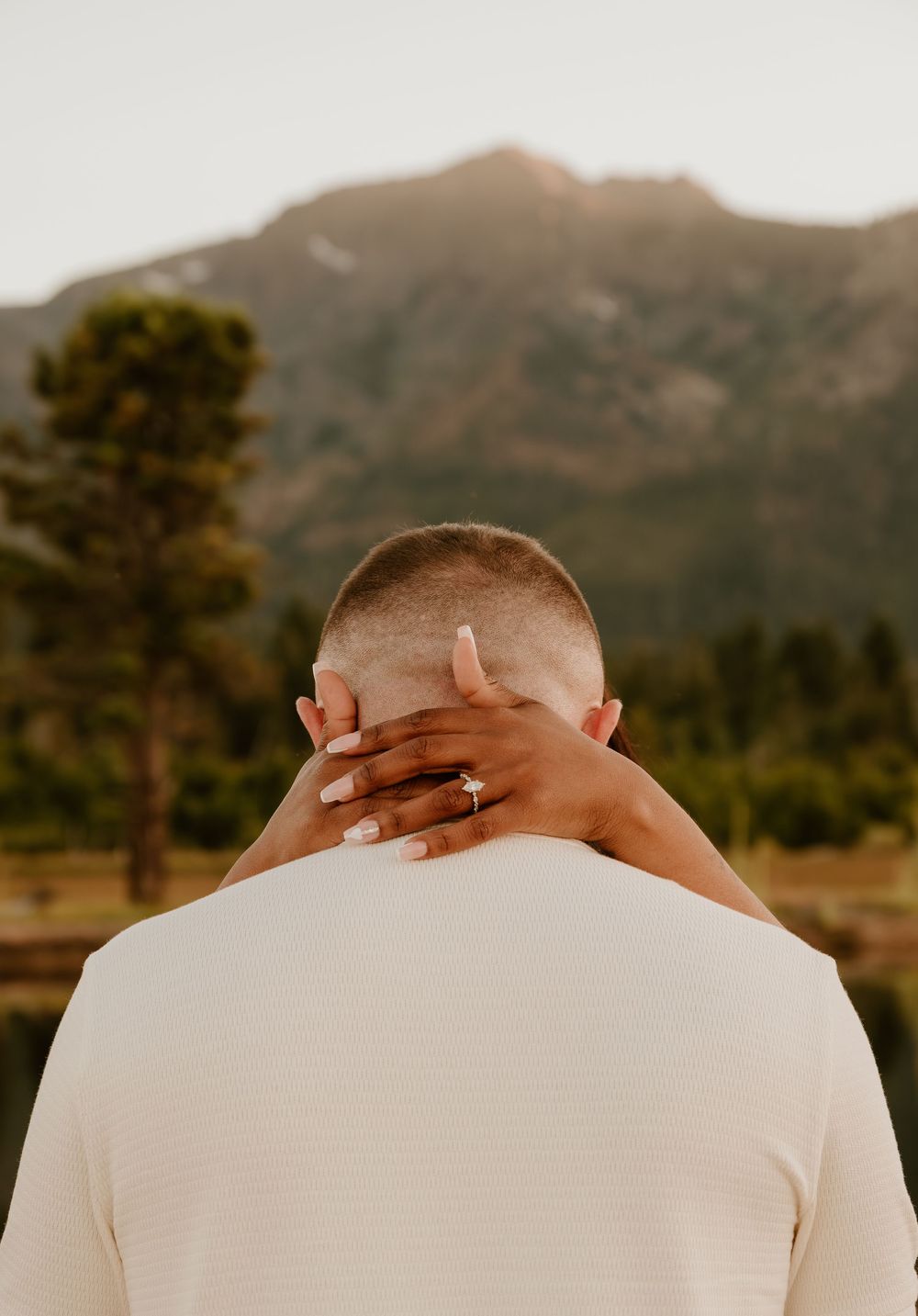 Back view of person in white shirt against mountain landscape at golden hour with hands clasped behind their neck.