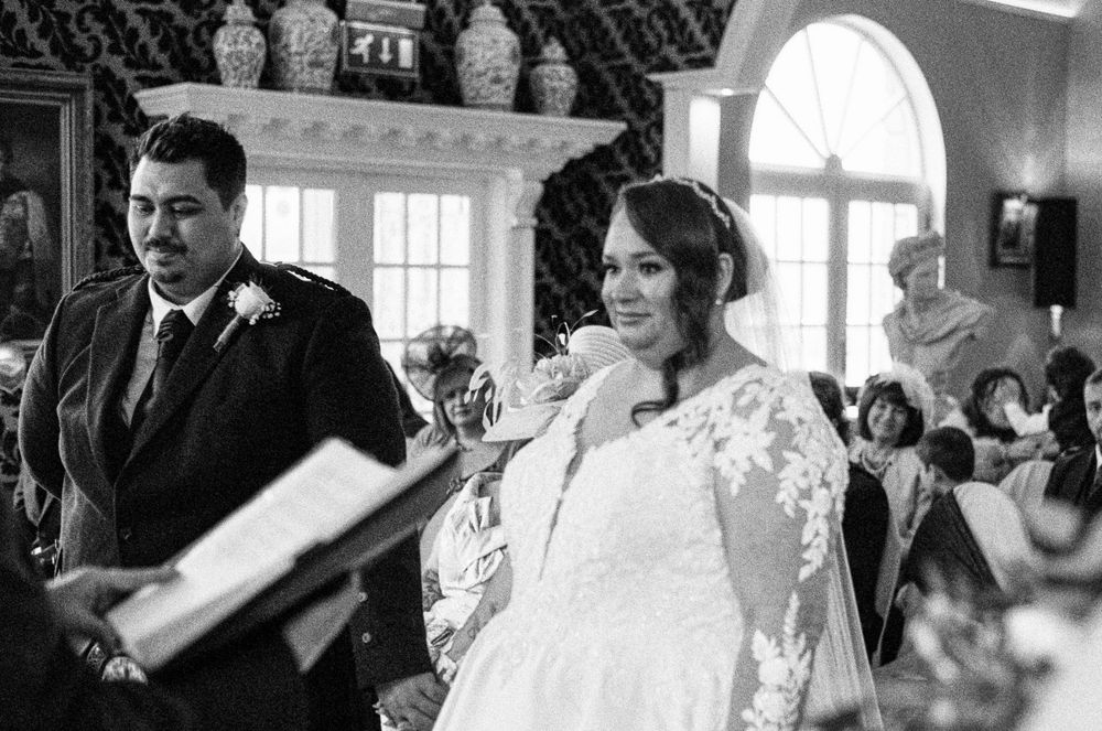 Elegant wedding ceremony in a grand venue with ornate columns and damask wallpaper.
