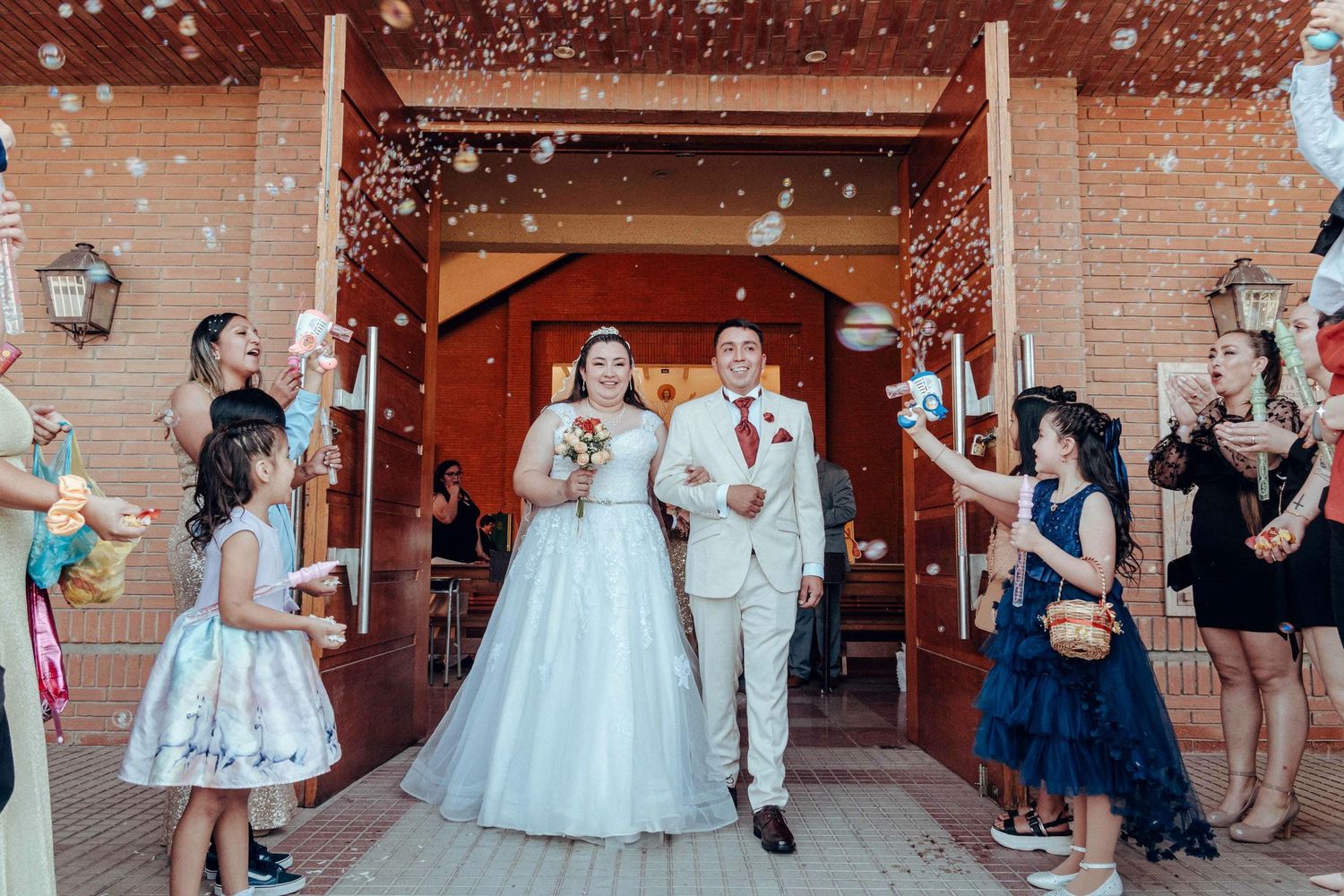 Salida de matrimonio con invitados lanzando confeti frente a entrada de edificio de ladrillo.