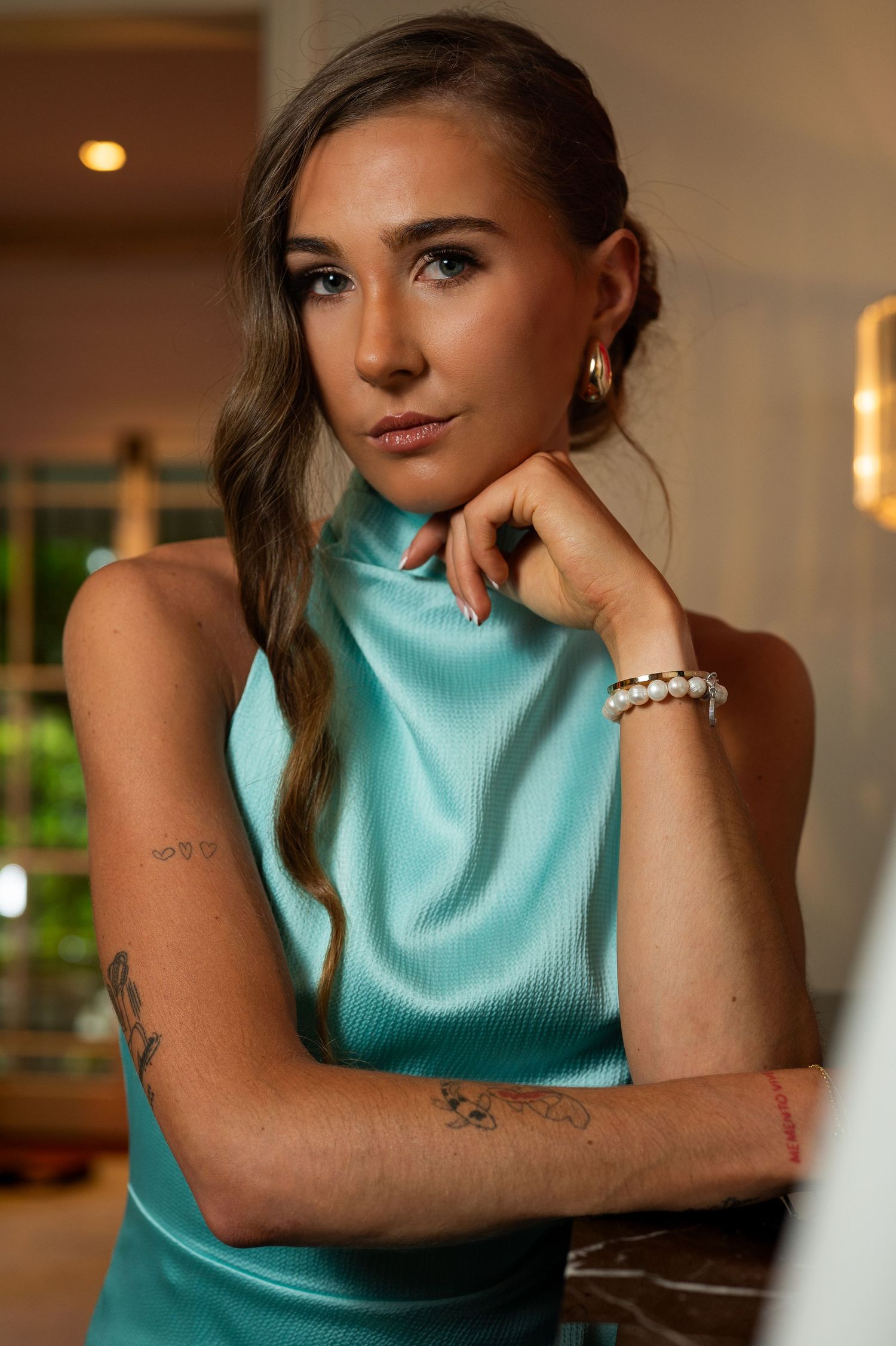 Portrait of woman in turquoise sleeveless turtleneck top with pearl bracelet in warm indoor lighting.