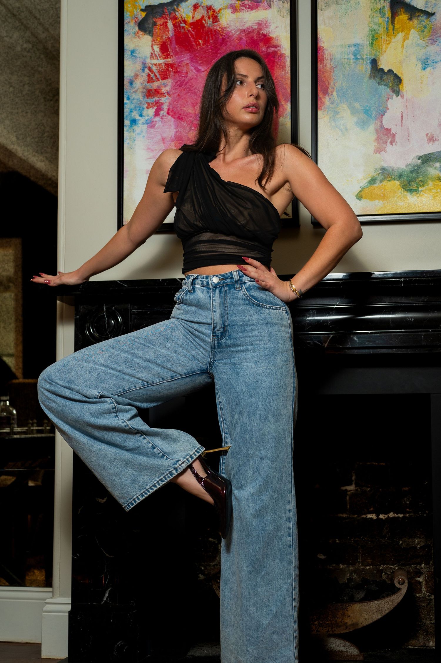 Fashion model poses in black crop top and wide-leg jeans against colorful abstract art wall.