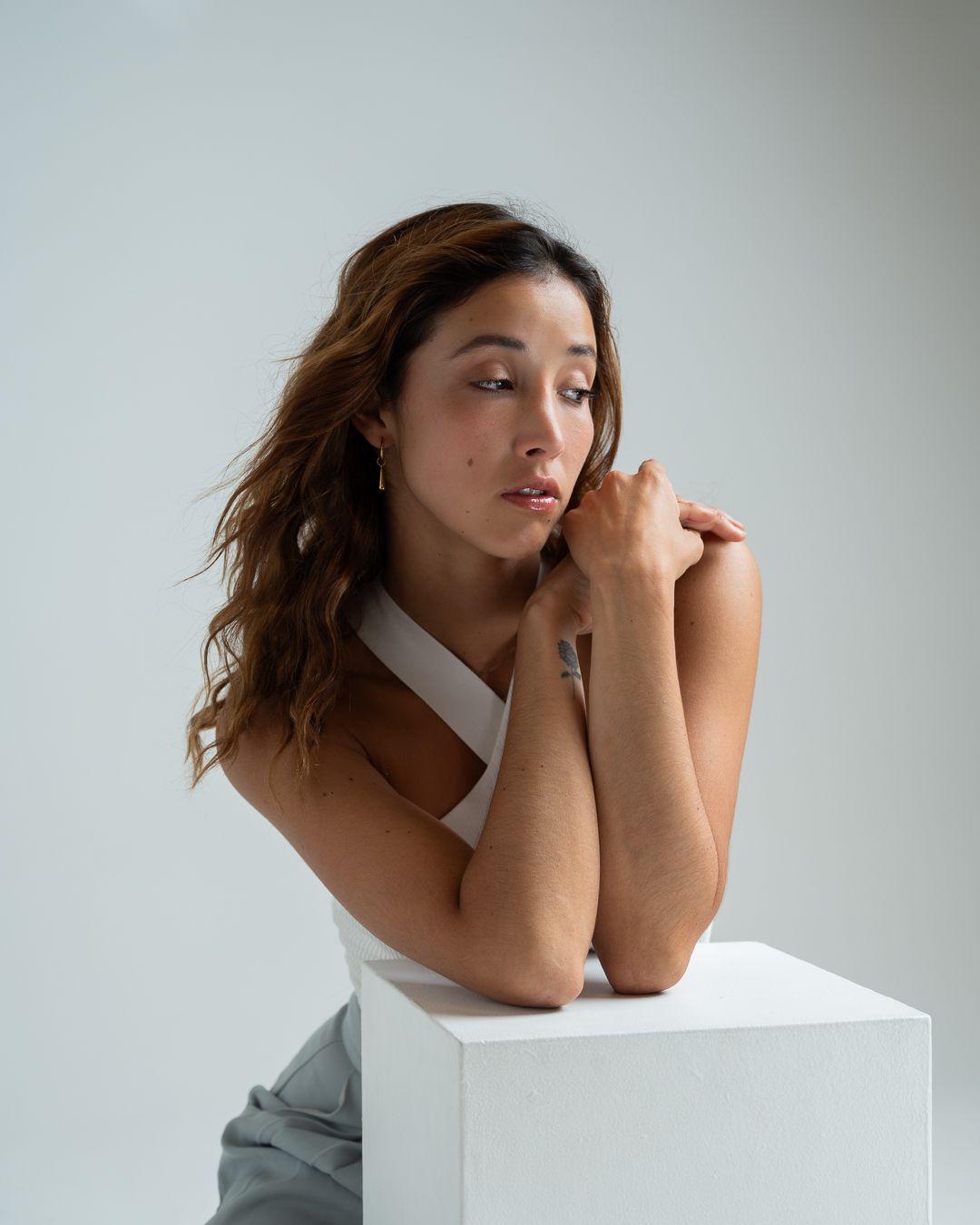 Person in white top and gray pants poses thoughtfully against neutral background in artistic portrait series.