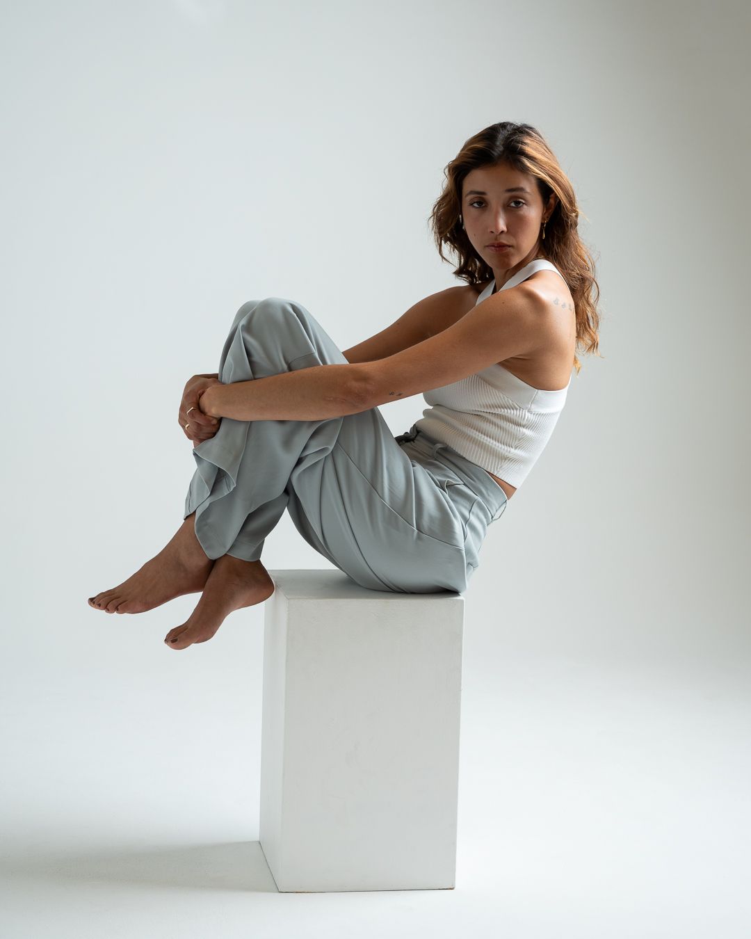 A minimalist photo series shows a person in white clothing posed artistically against a white cube and wall.