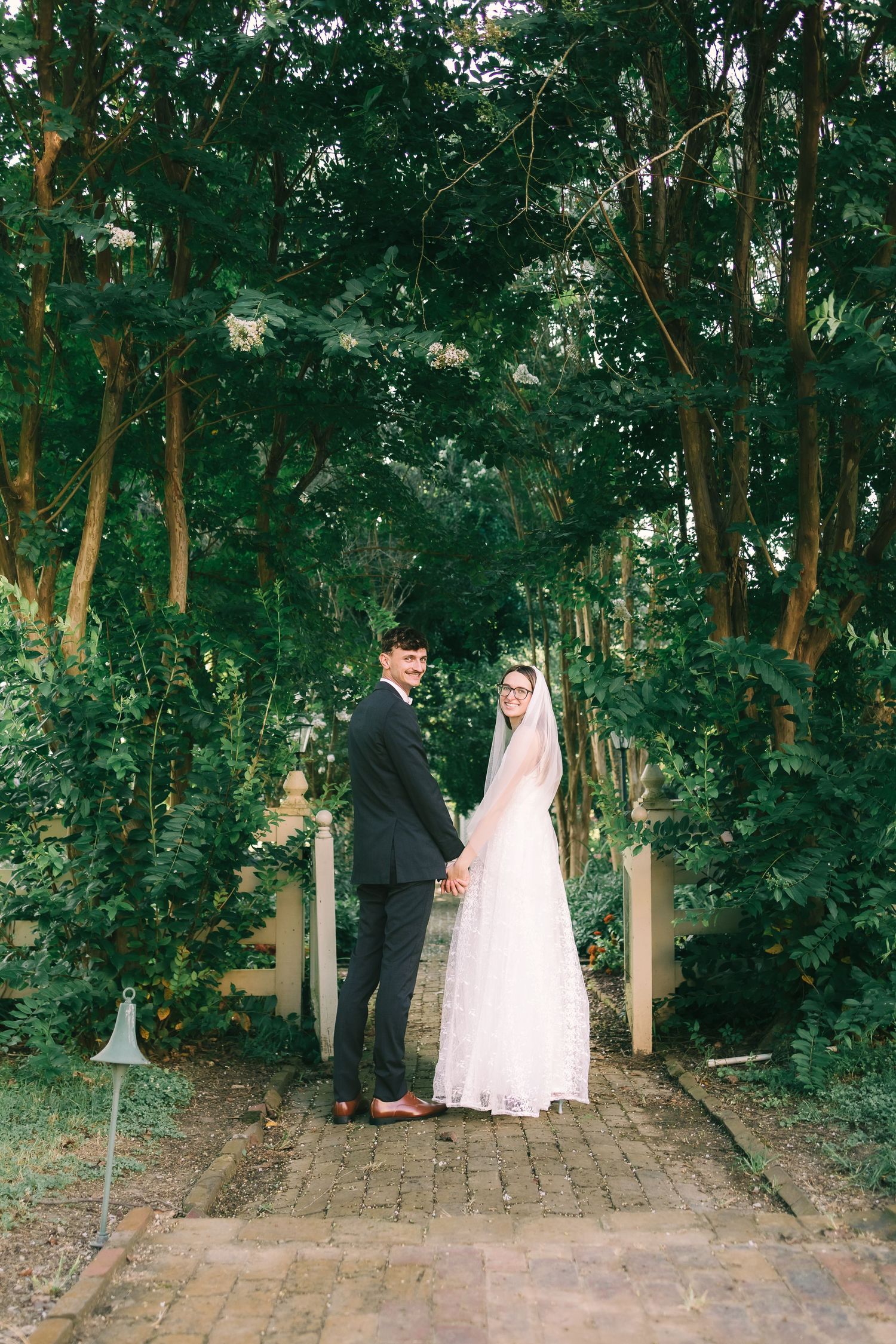 A couple in wedding attire shares a romantic moment on a stone path surrounded by lush green trees in the forest.