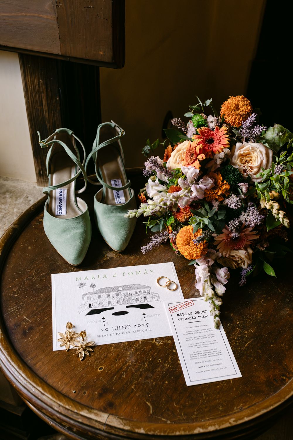 Wedding details including mint green shoes, colorful floral arrangements, and invitation cards displayed on a wooden table in alenquer