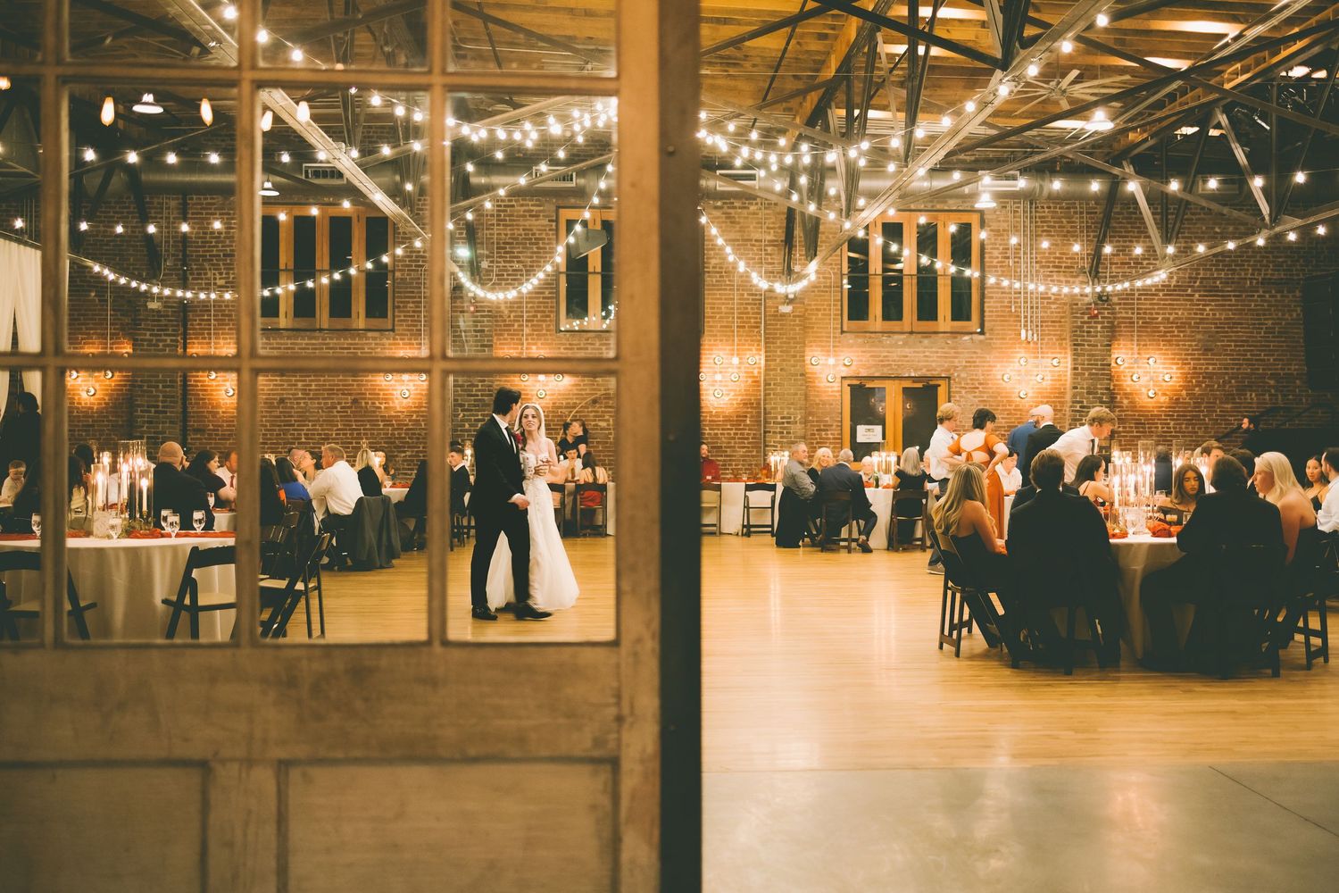 Rustic indoor wedding venue with string lights and wooden beams creating a warm, romantic atmosphere.