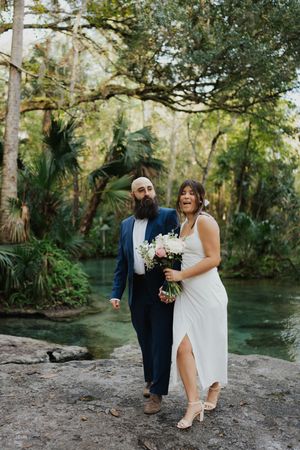 A couple shares a joyful moment together by a scenic river in a lush, tropical forest setting.