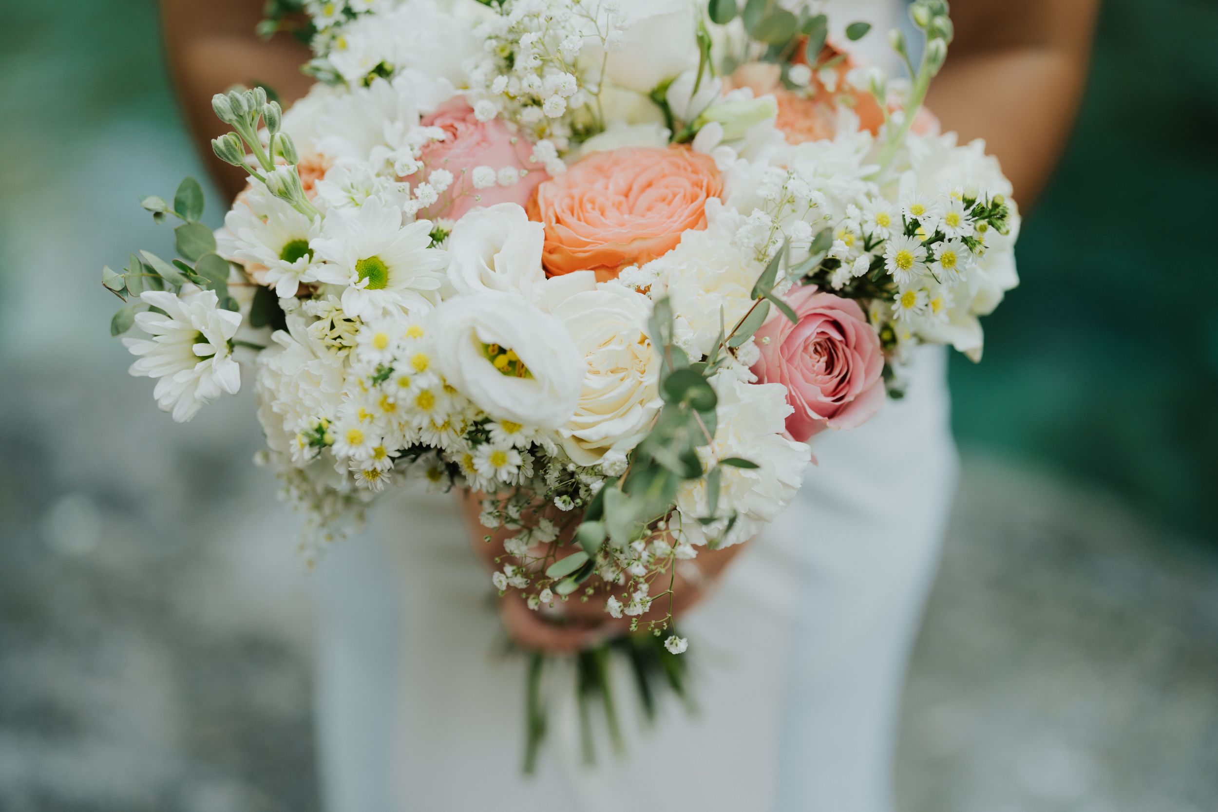 Delicate white and pink floral wedding bouquet with roses and baby's breath against a soft teal background.