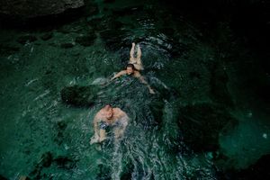 Underwater view of a swimmer gliding through dark turquoise water creating rippling patterns and bubbles.