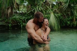Couple embracing in turquoise tropical waters surrounded by lush palm trees and jungle vegetation.