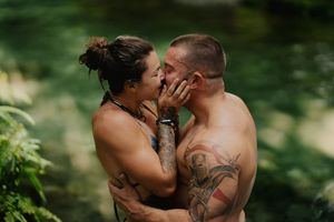 A romantic outdoor portrait of a couple embracing in a natural setting with green foliage in the background.