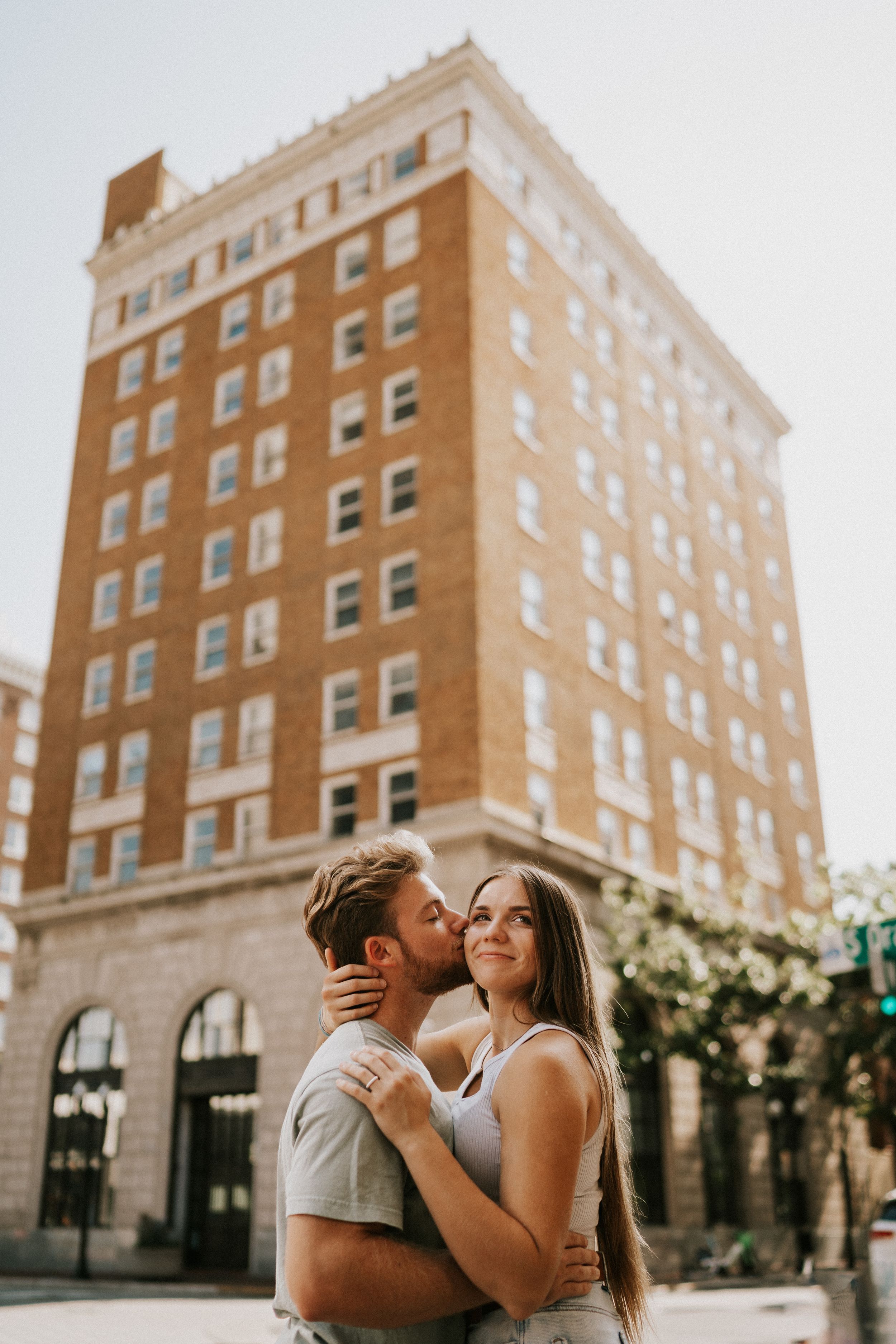 Couple embracing and laughing together outside a historic brick apartment building on a sunny day.