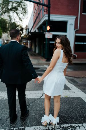 A couple in formal attire playfully poses on a city street during a photo session.