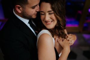 Couple shares intimate dance moment at wedding reception with purple and blue lighting in background.