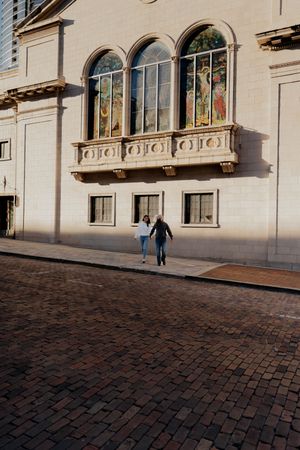 Ornate building facade with arched windows and flower boxes along a cobblestone street in warm sunlight.