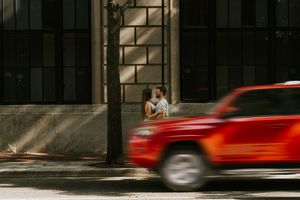 A motion-blurred red car speeds past a building entrance on an urban street.