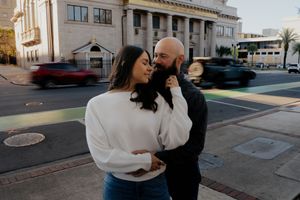 A couple shares an intimate moment on a city street corner with a classic building facade in the background.