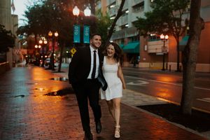 A couple walks along a city street at dusk with glowing street lamps creating a romantic urban atmosphere.