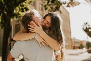 A romantic couple embraces and kisses in a warm outdoor setting during golden hour.
