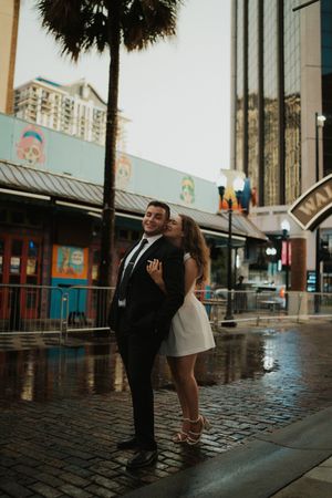 A couple dances together on a wet cobblestone street in front of urban storefronts.