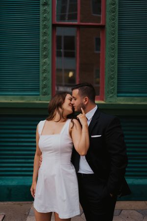 Romantic couple sharing an intimate moment against a green building exterior.