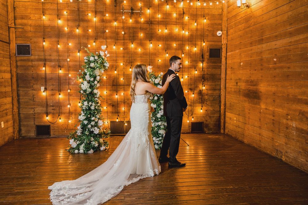 A romantic wedding scene with a decorated Christmas tree and twinkle lights illuminating a rustic wooden barn interior.