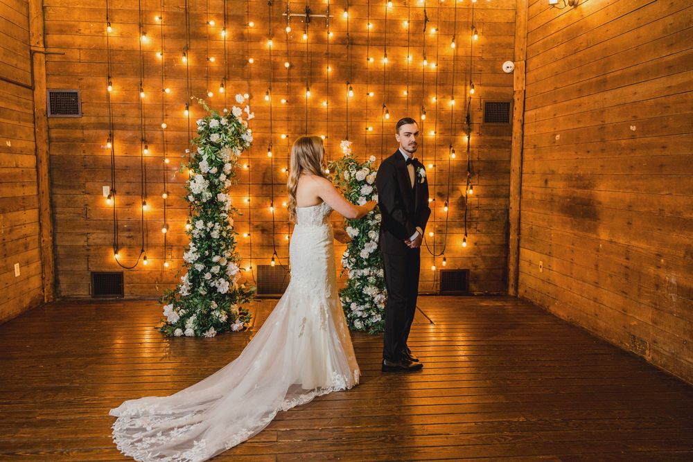 A rustic barn wedding ceremony space with wooden walls, string lights, and a decorated Christmas tree in the corner.