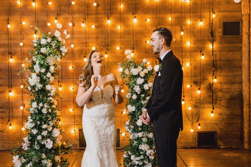 Couple sharing a romantic moment in rustic barn venue with warm string lights and floral arrangements.
